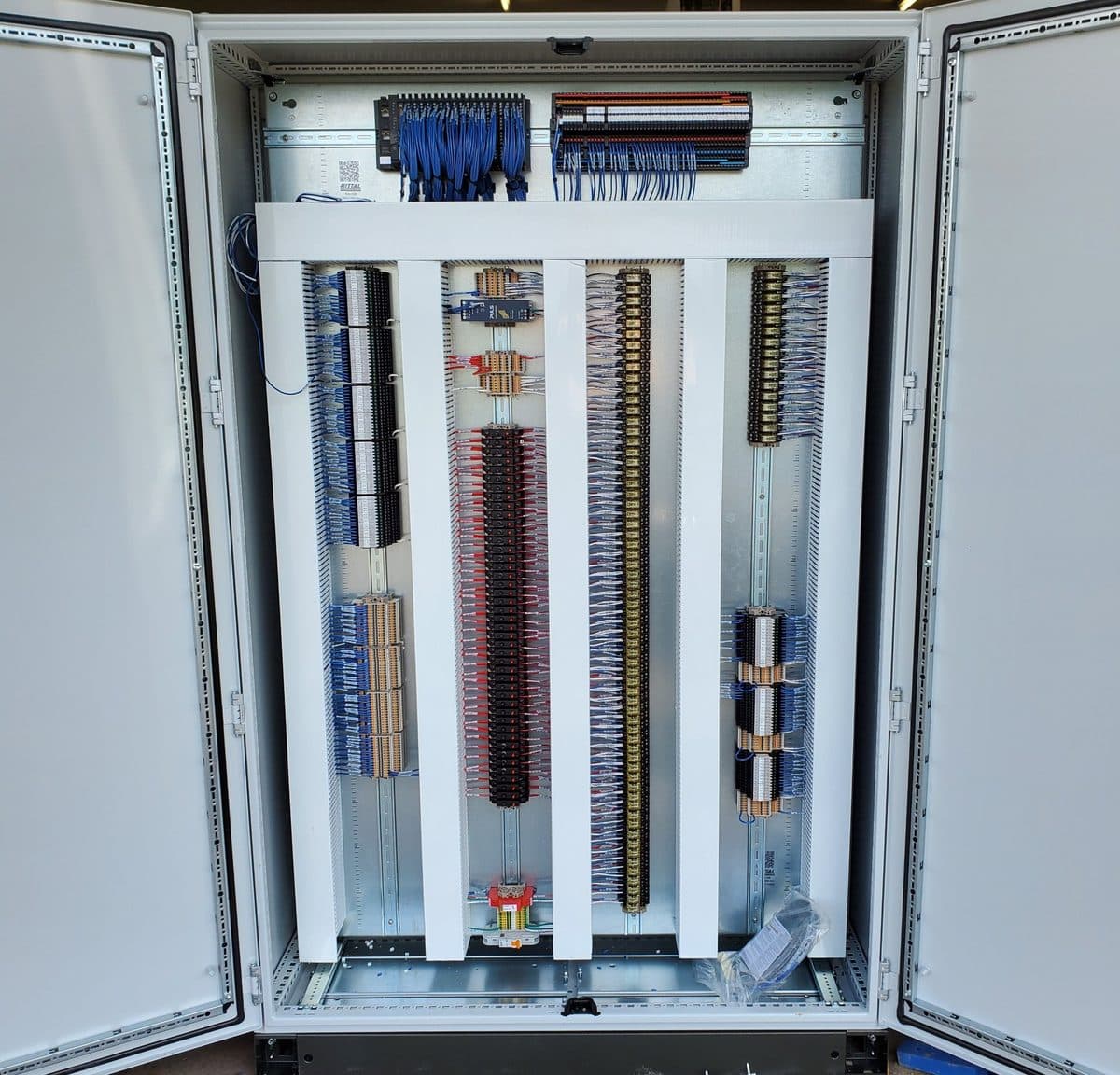 A large double-door control panel with both doors open: a remote I/O system and DC circuit breakers across the top, then a DC power supply, a column of ice cube interposing relays, double-level terminal blocks and banks of slimline relays, with incoming power, a circuit breaker and surge protection at the bottom, all with labeled wiring.