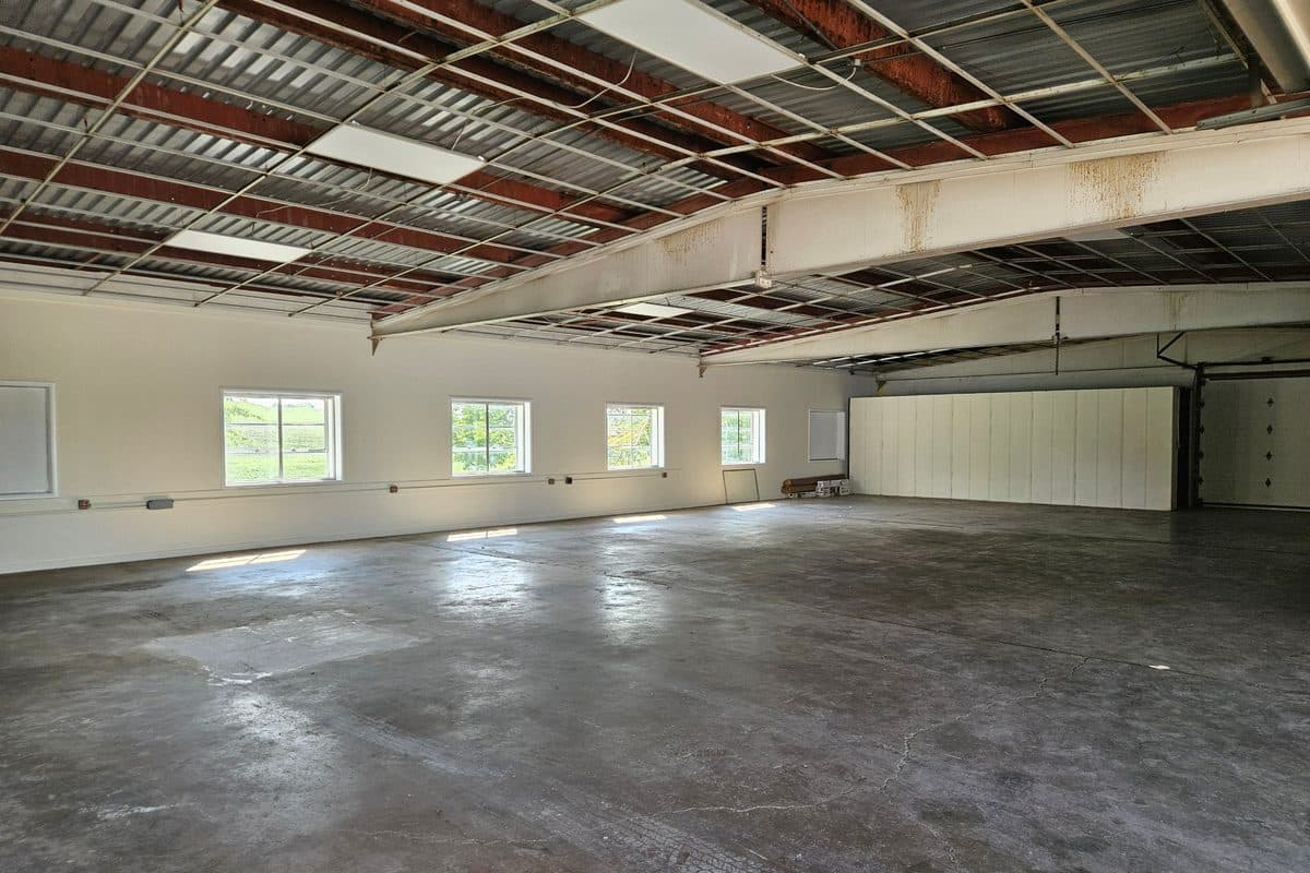 Inside the new manufacturing space: an open concrete floor under a steel truss roof, with a row of windows along one wall and an overhead door.