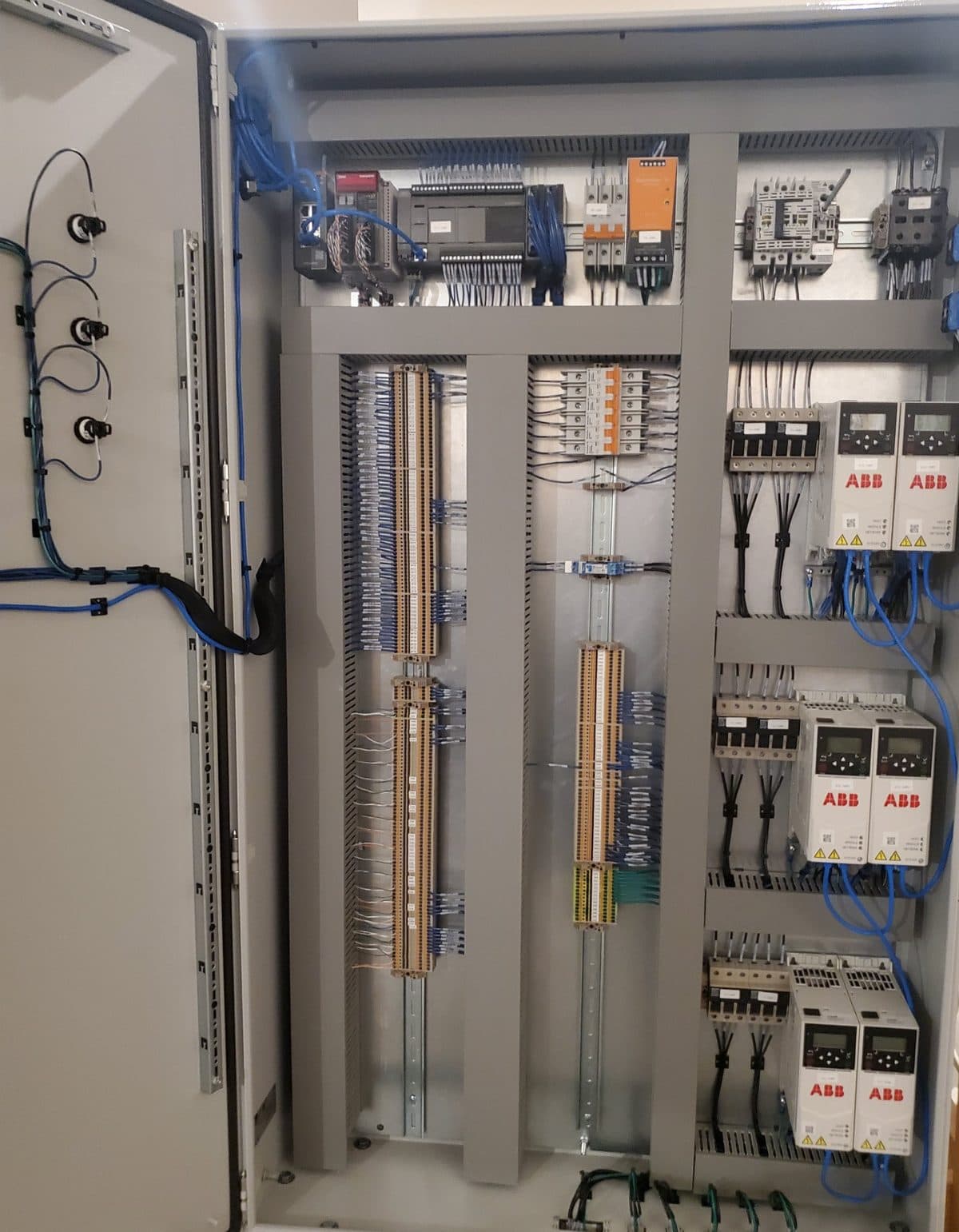 A floor-standing control panel for a fully automated TAB wrapping system with its door open: three operator devices and neatly bundled wiring on the door, an Ethernet switch, IDEC PLC, circuit breakers and power supply across the top, columns of labeled terminal blocks in the middle, and six variable frequency drives on the right.