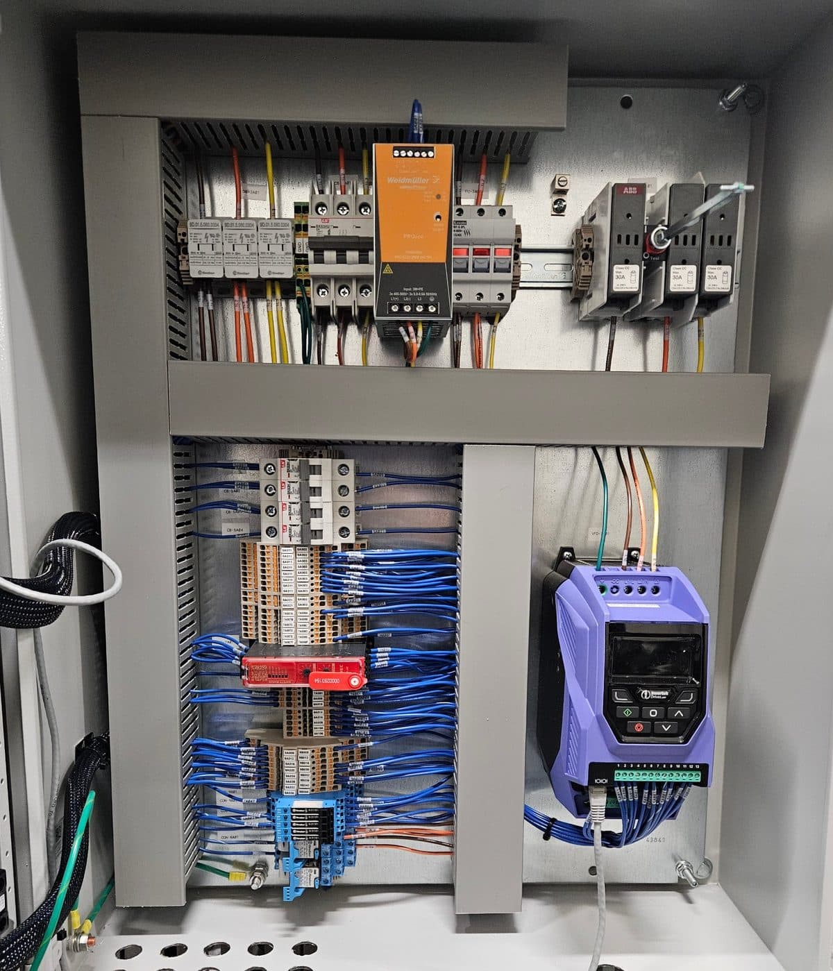 Inside a TAB WRAPPER TORNADO Genius controls panel mounted on the machine: power supply and fuses across the top, labeled terminal blocks, an IDEC safety relay and interface relays in the middle, and a variable frequency drive on the right.